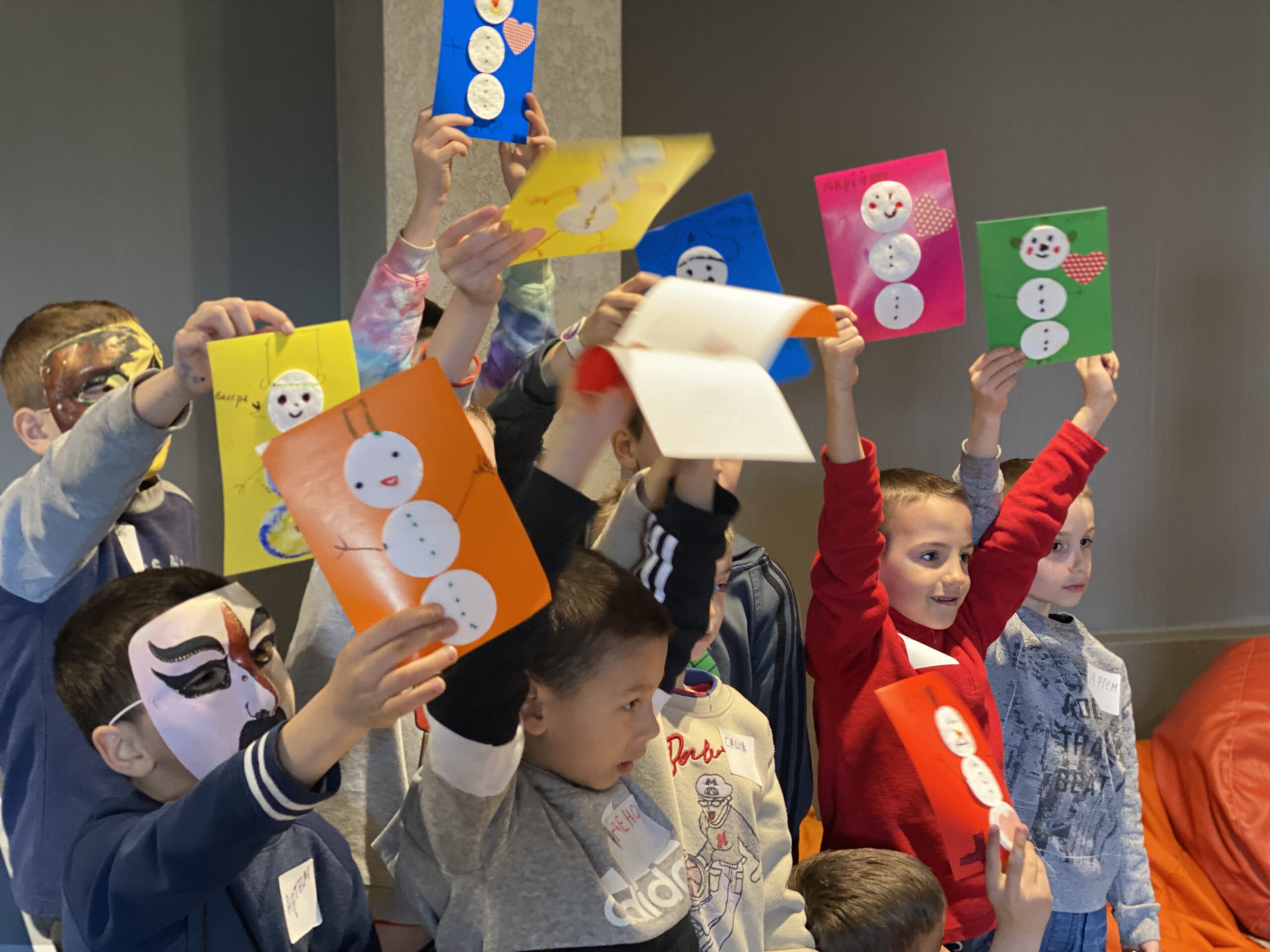 Grupa dzieci podnosząca nad głowy rysunki bałwanków