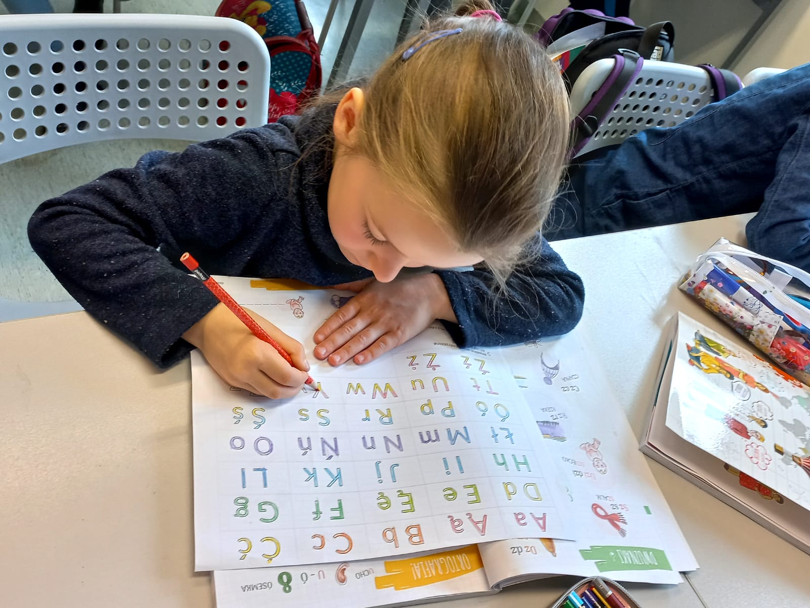 Dziewczynka kolorująca litery alfabetu na kartce